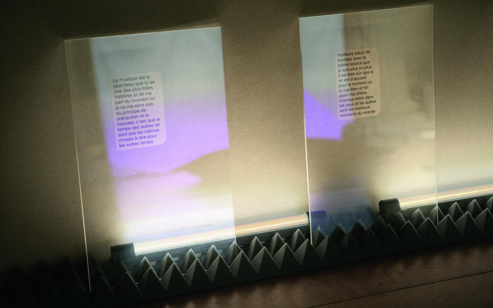Zwei transparente Glasplatten sind in Noppenschaumstoff einglassen. Auf ihnen französische Texte in Sprechblasformen zu sehen. 
