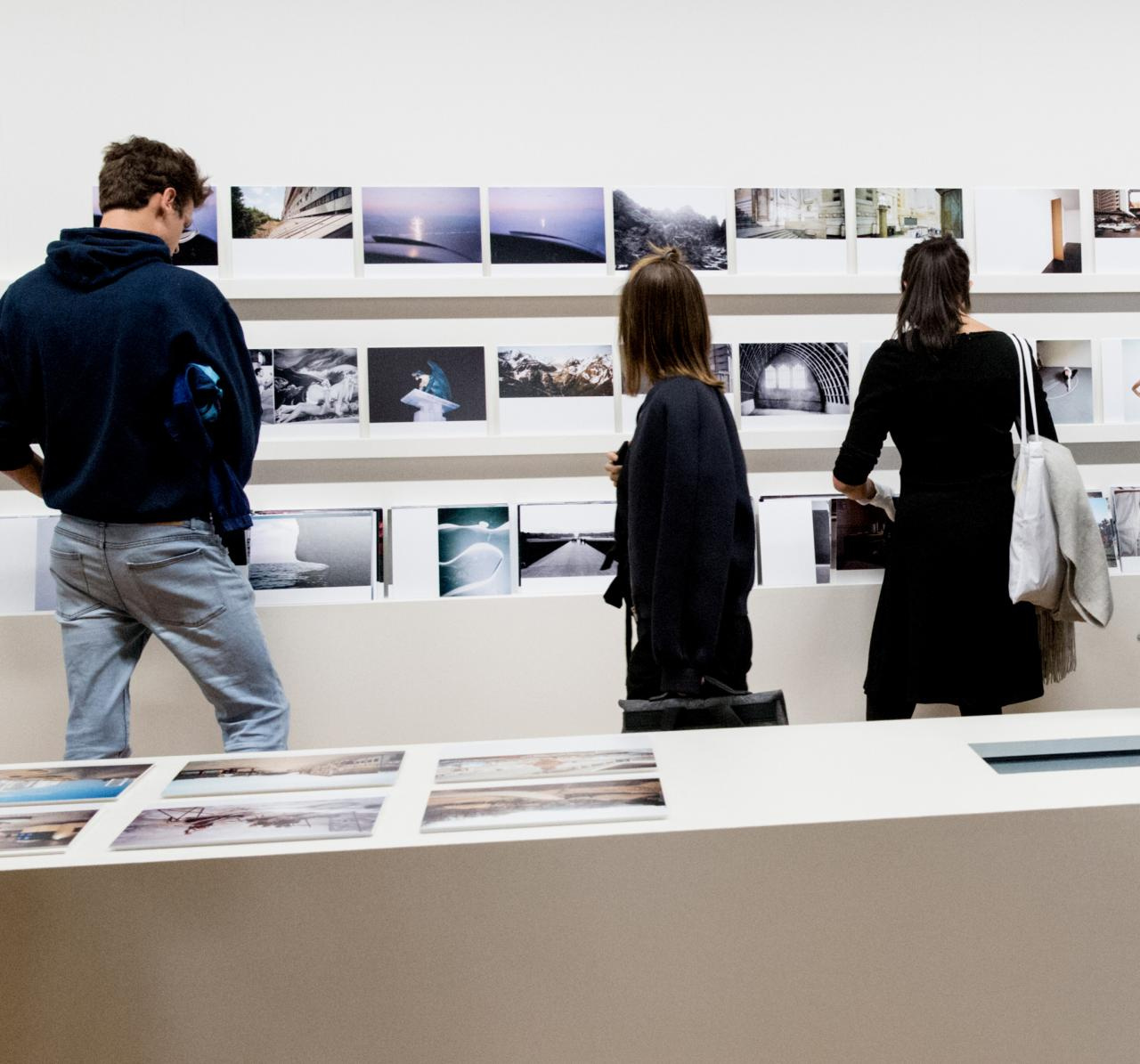 Three people view photographs in an exhibition