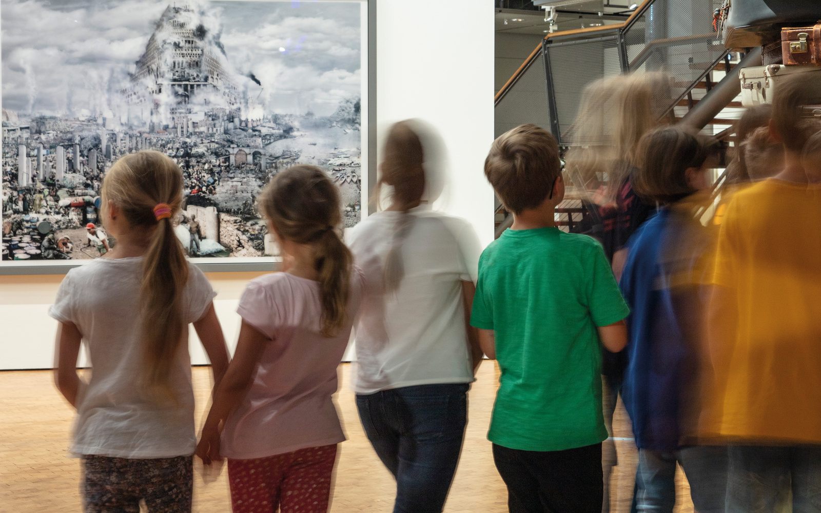 Zu sehen sind eine verschommene Gruppe Kinder vor einem Bild, welches den Turm zu Babel zeigt.