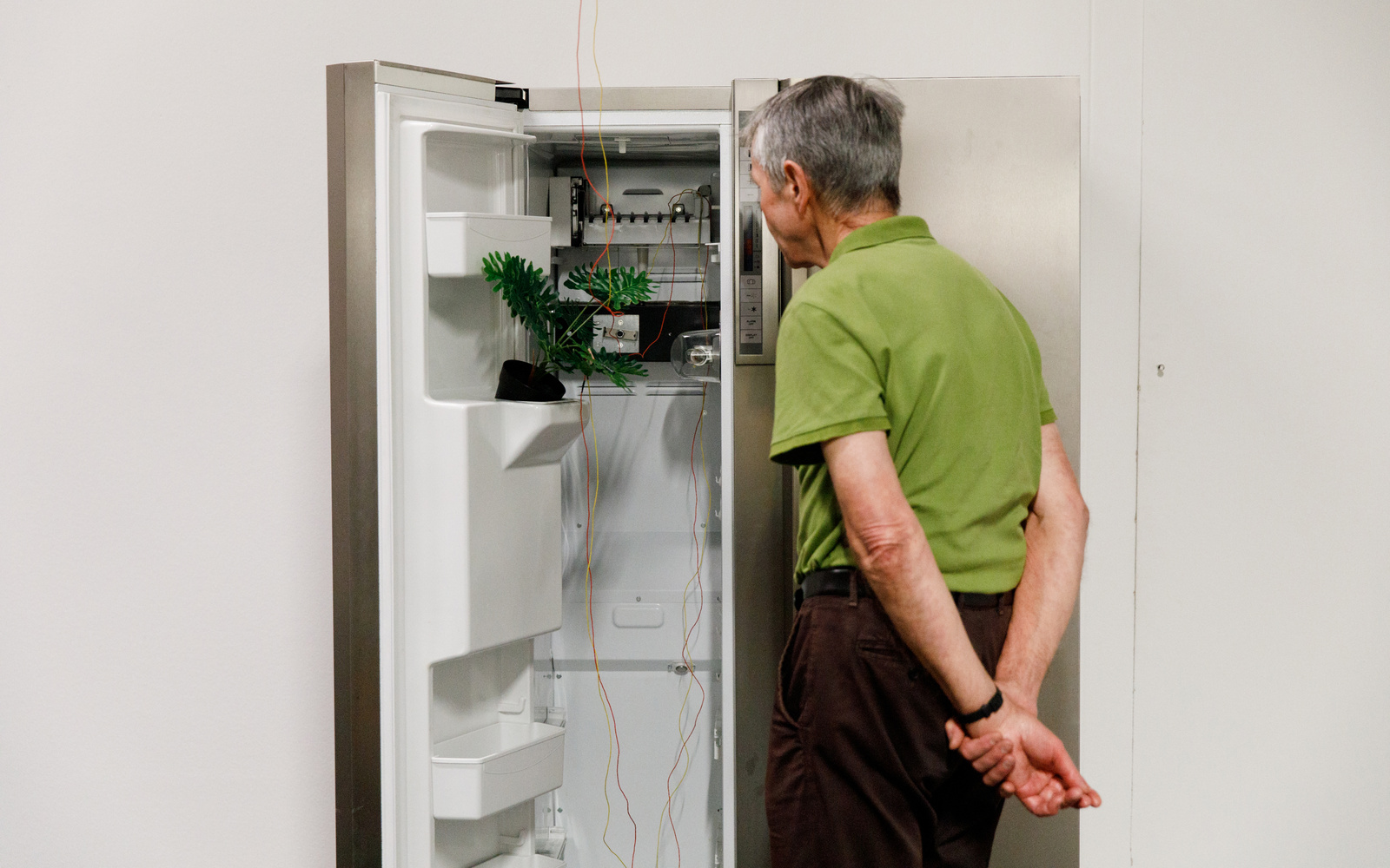 An elderly gentleman stands in front of an open refrigerator, which has been converted into a media installation. 