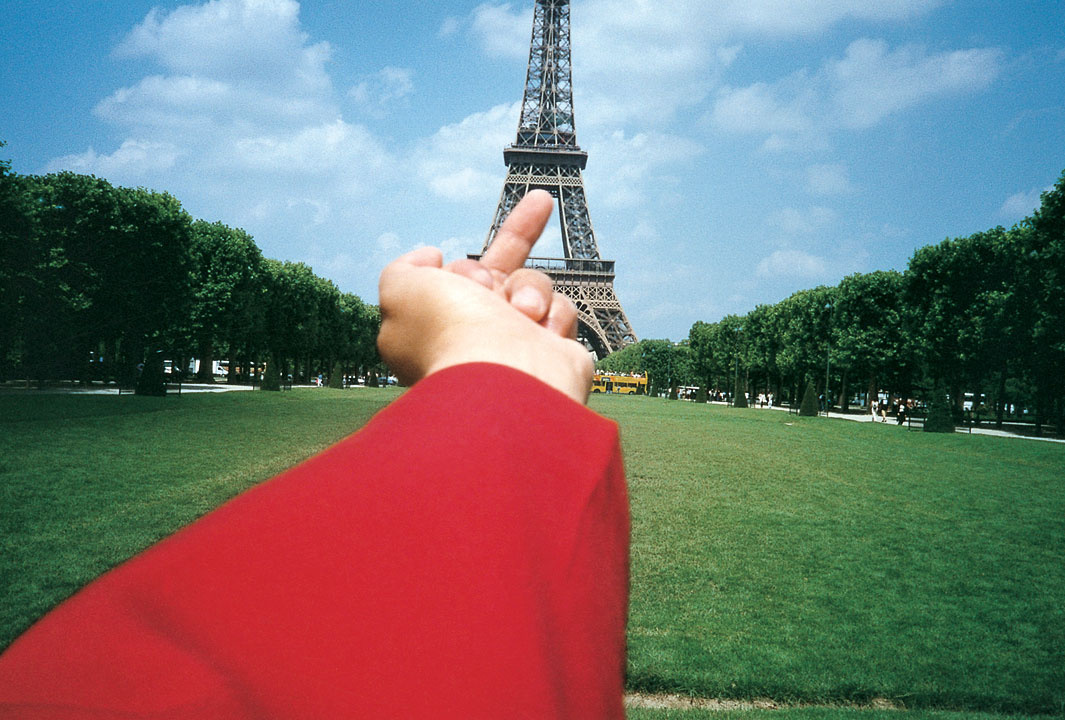 Zu sehen ist ein ausgestreckter roter Ärmel, der den Mittelfinger auf den Eiffelturm zeigt