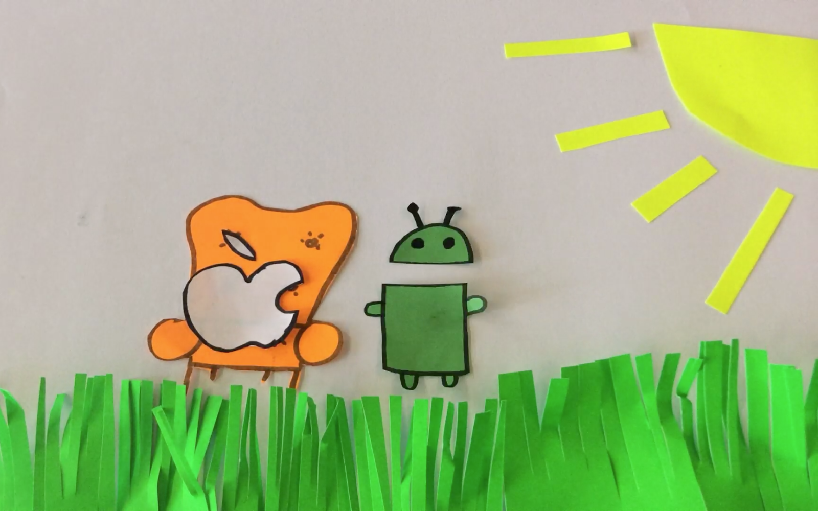 Standbild eines Trickfilms auf dem der abgebissene Apfel von Apple neben dem Maskottchen von Android auf einem Sessel sitzt.