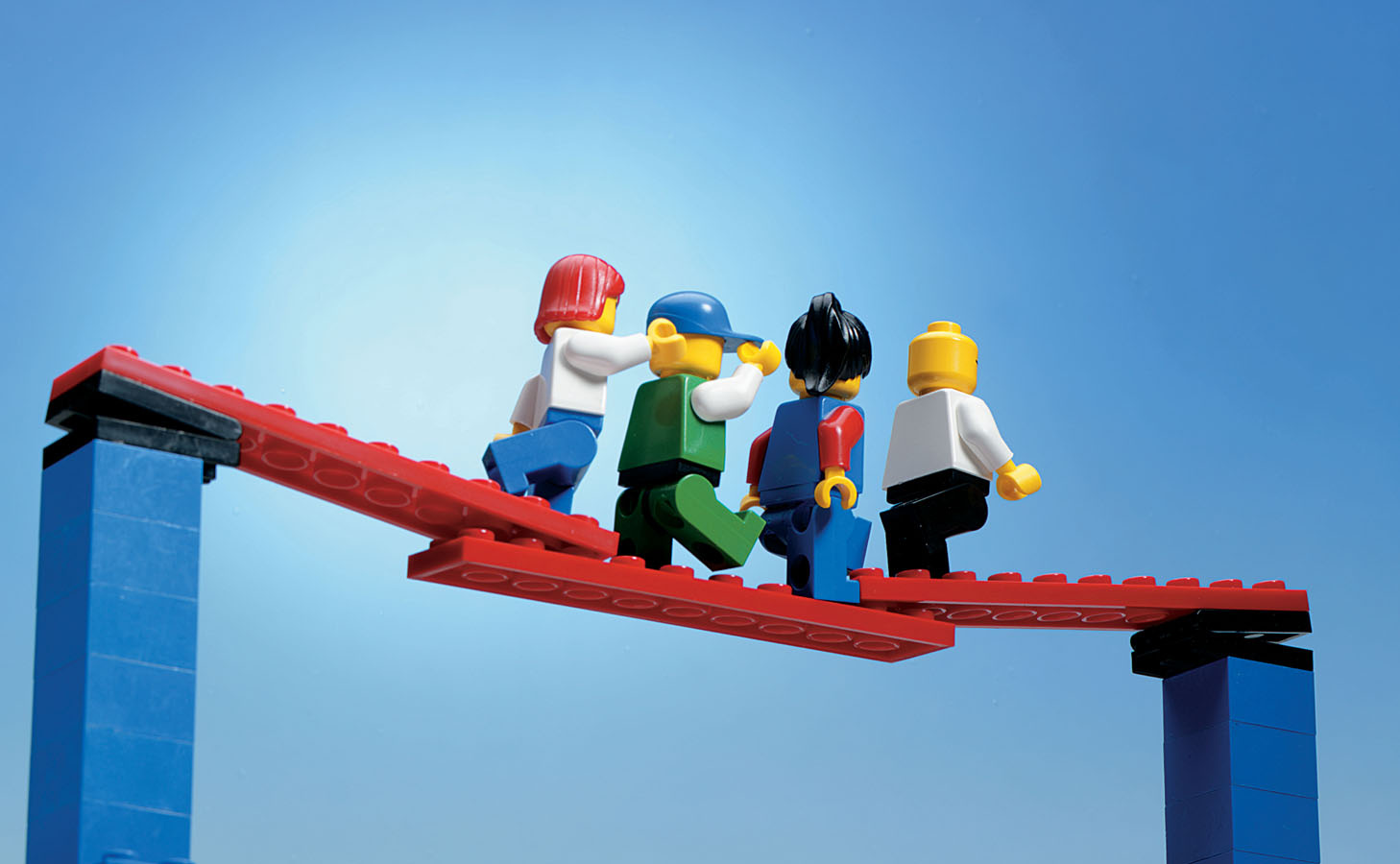 Four Lego figures in a row cross a bridge.