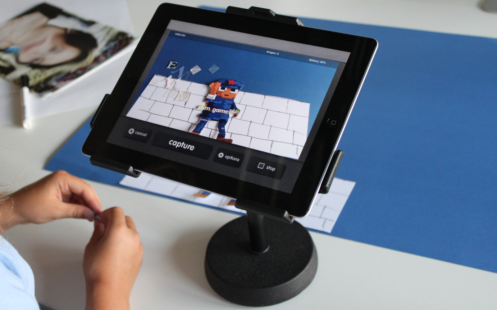 Man sieht zwei Kinderhände, die an einer Papiercollage arbeiten, die mit dem iPad zum Stop-Motion-Trickfilm wird. 