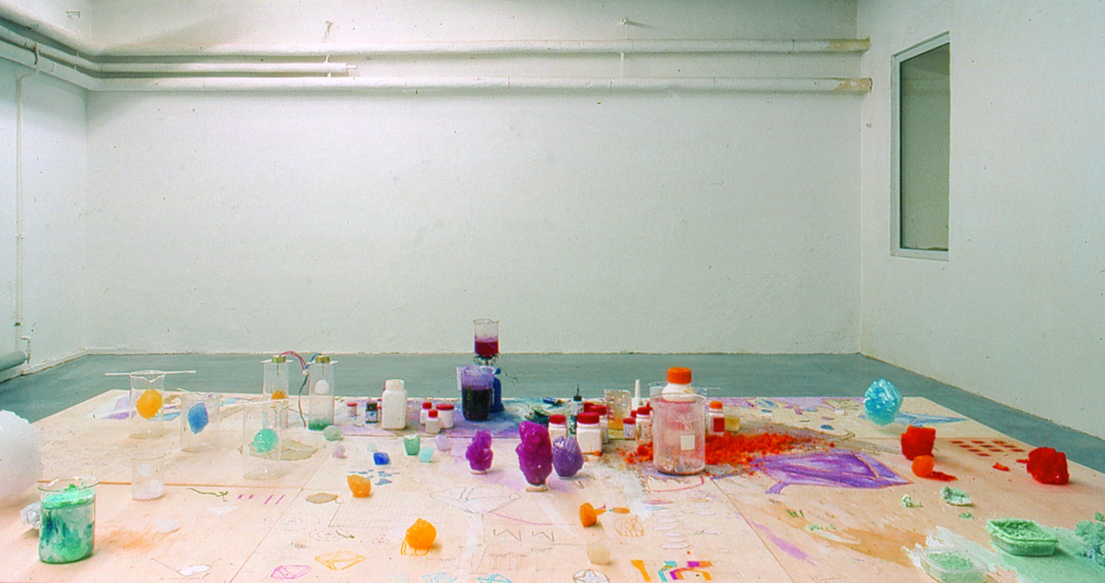 View of the exhibition "Fiction & Science». In the foreground a table with colorful crystals and chemicals.