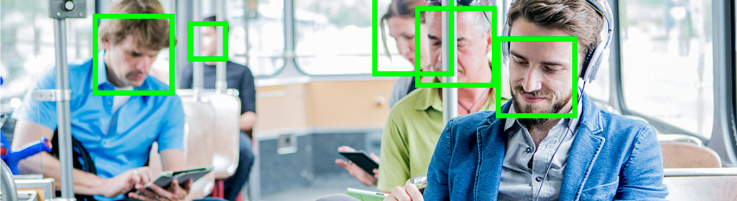 The photo shows several people in a tram, all looking at their smartphone. Above their faces lies the face recognition symbol in neon green color.