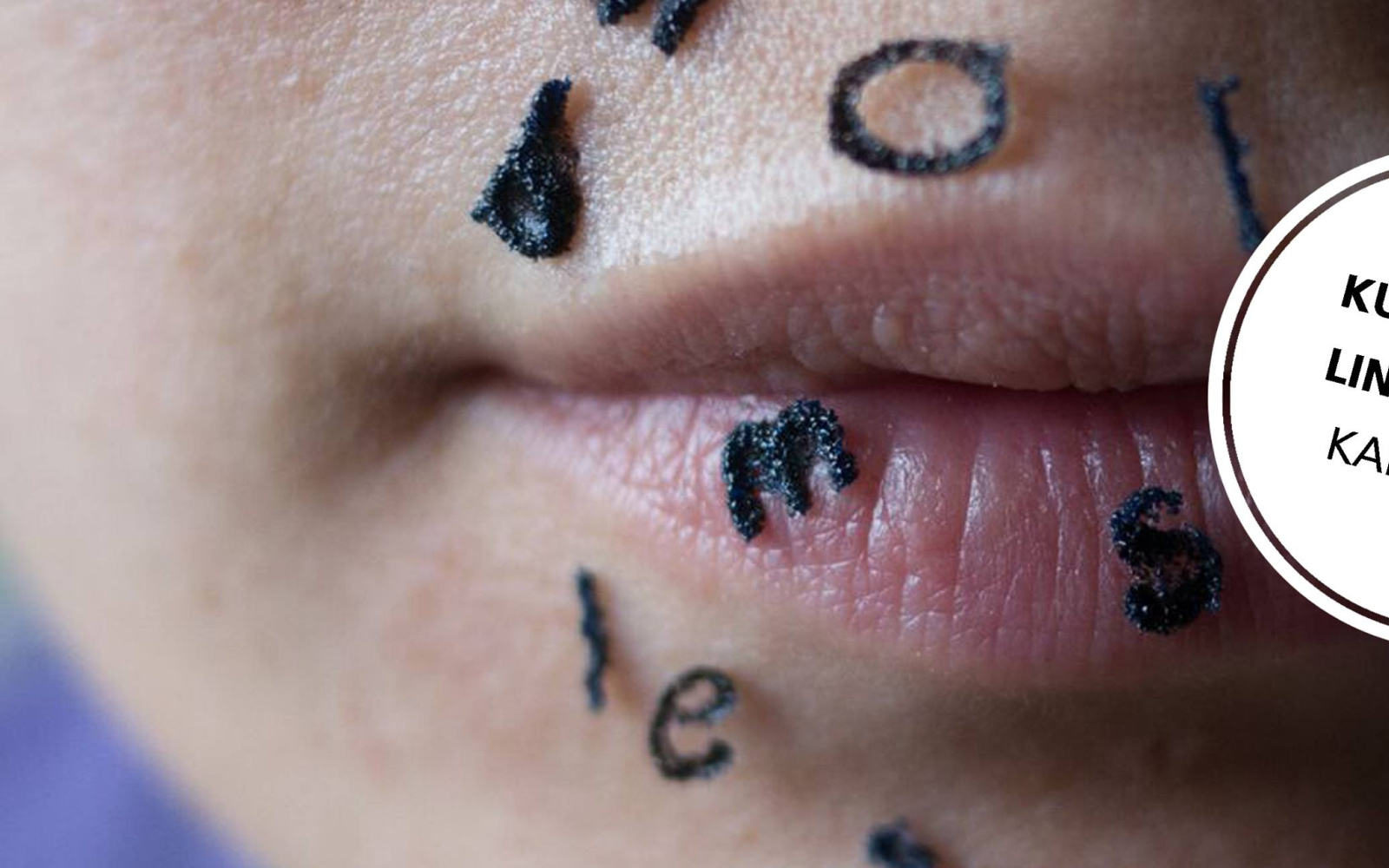 Close-up of a mouth with painted black letters on the skin.