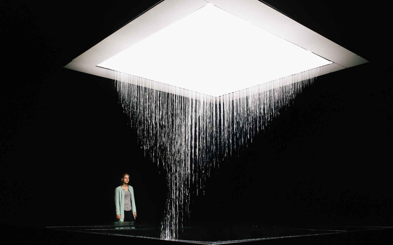 Photo of the installation 3D WATERMATRIX in which water falls to the ground and generates 3D shapes. A person is watching the insatallation.