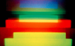 A holographic image by Dieter Jung. Red, blue, green and yellow horizontal stripes on a dark background.
