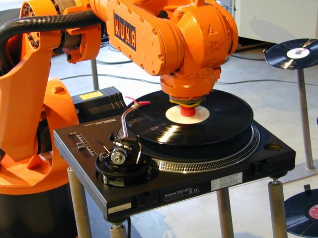 An orange robot arm puts on records.