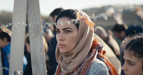 A woman with a headscarf is standing behind a barbed wire fence.