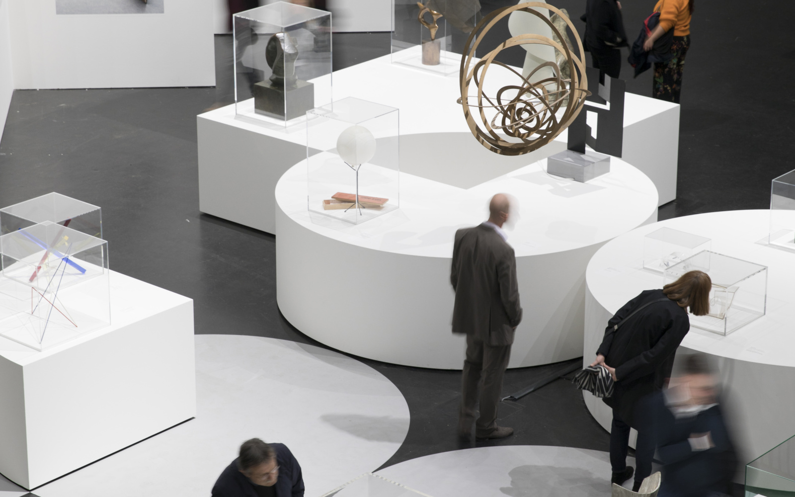 Sculptures stand on white pedestals, visitors are on their way in between.
