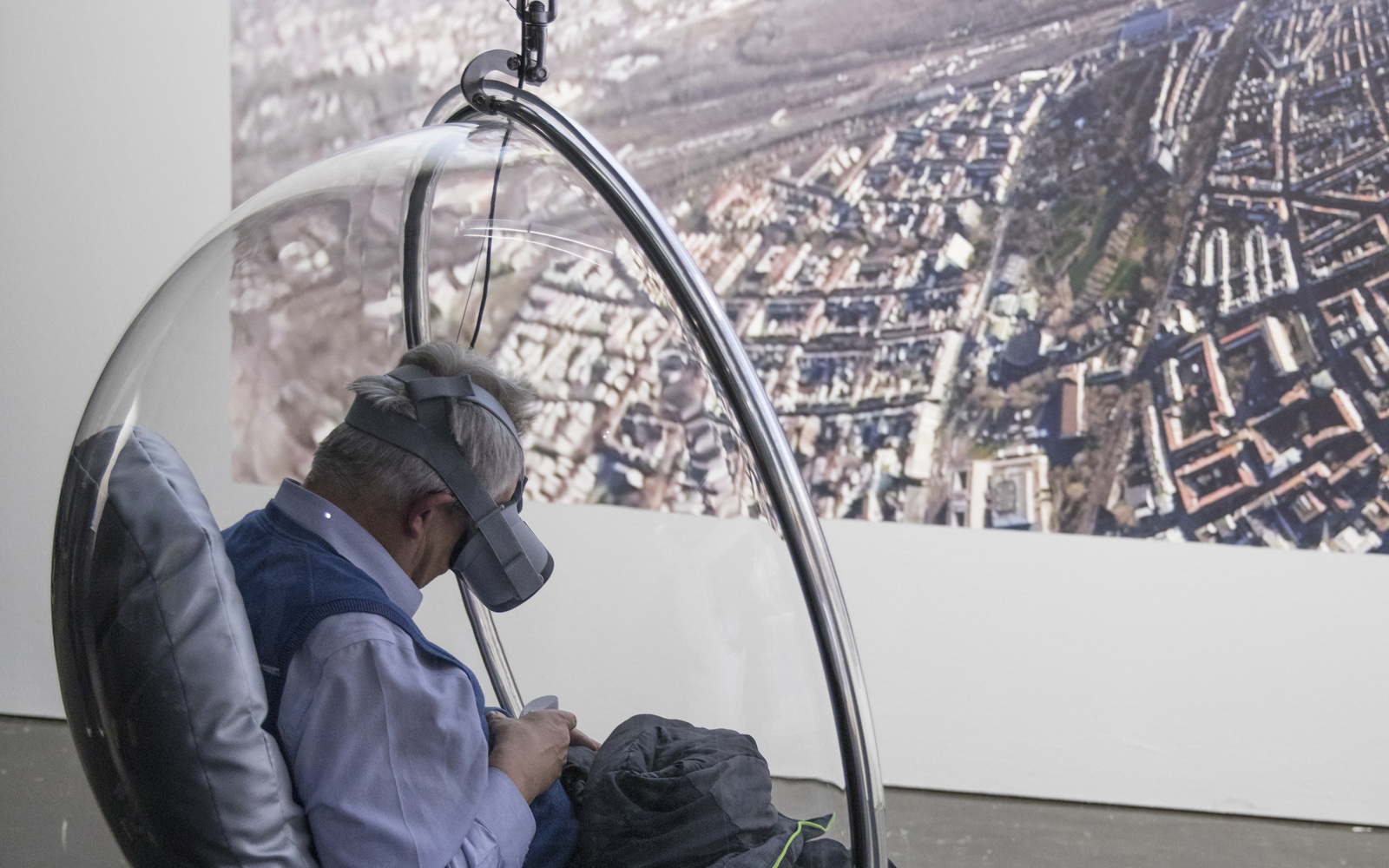 Ein Besucher mit VR-Brille sitzt in einem hängenden halbrunden Sessel aus durchsichtigem Kunststoff.