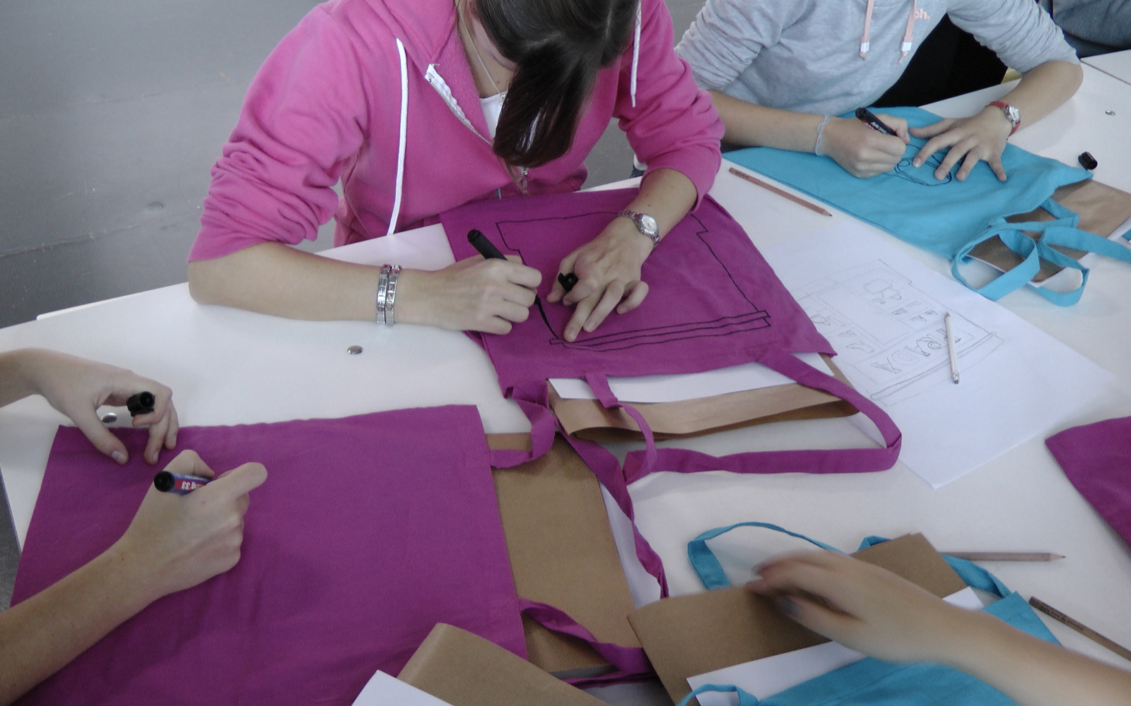 Kids are writing funny slogans on tote bags in front of them.