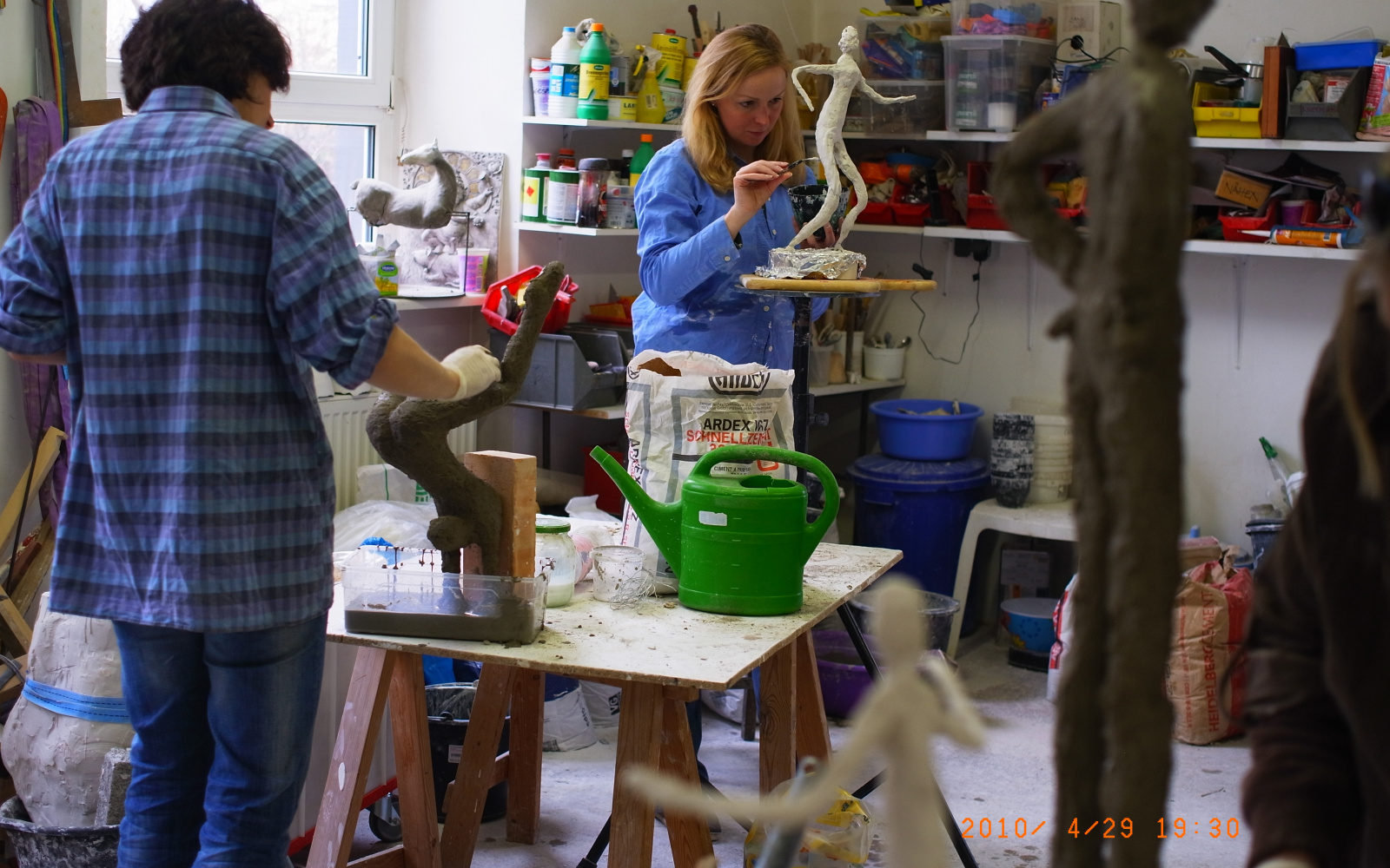 Women in an atelier are workig on slender figurines out of gesso.