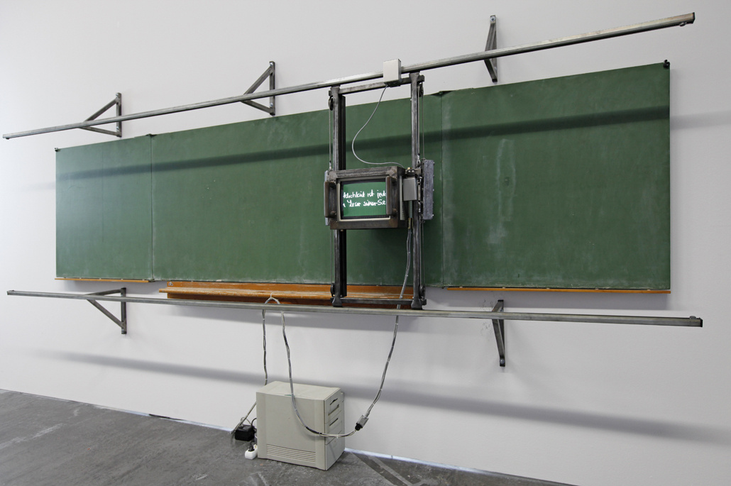 A monitor on rails in front of a blackboard
