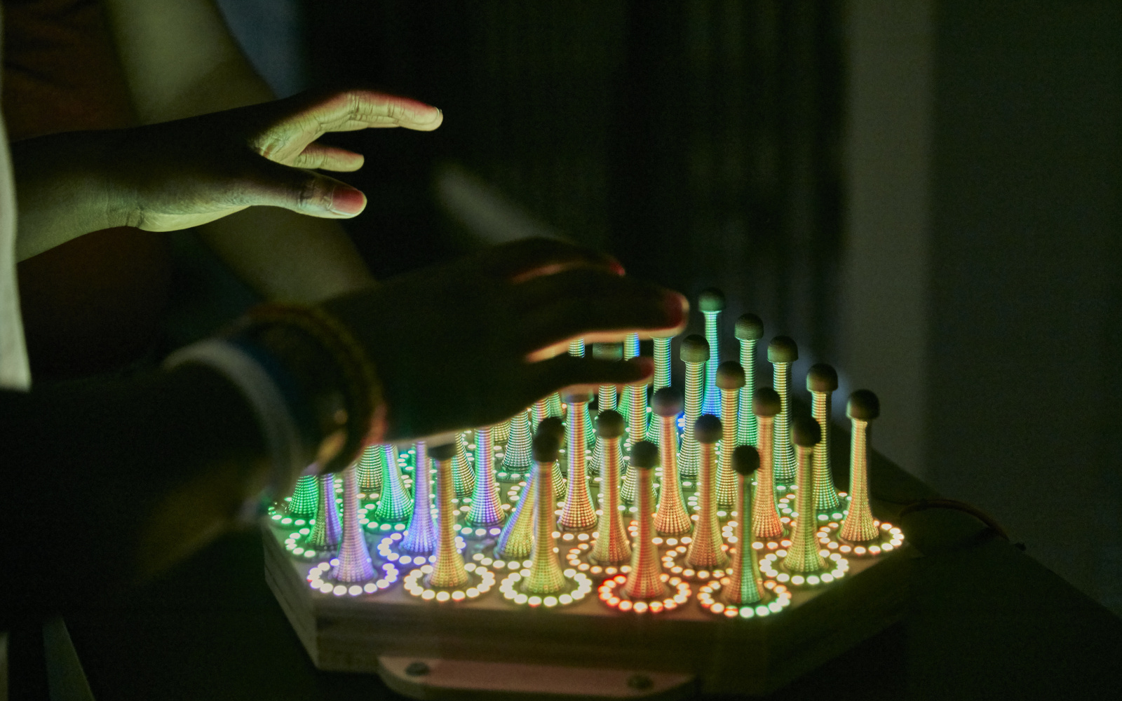 Hands above the artwork »Wobble Garden«, which consists of metal springs and LED circles.