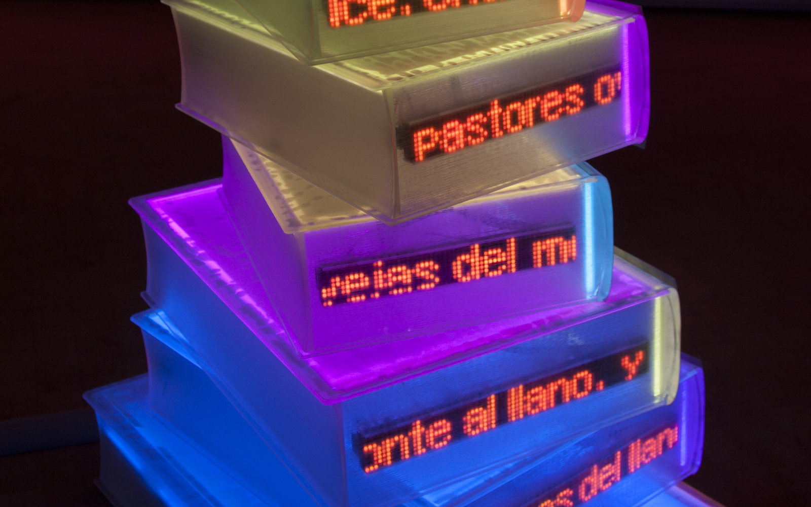 Colorfully illuminated books are stacked to form a sculpture.