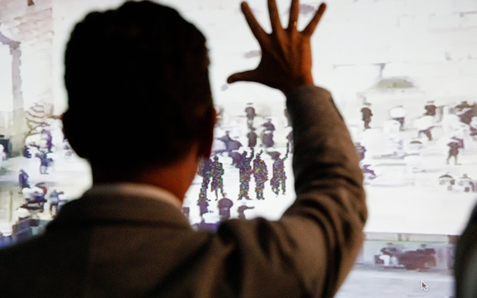 A picture can be seen on a wall on which shadowy figures raise their hands to salute. In front of it stands a man, his back to the observer and also raising his hand.