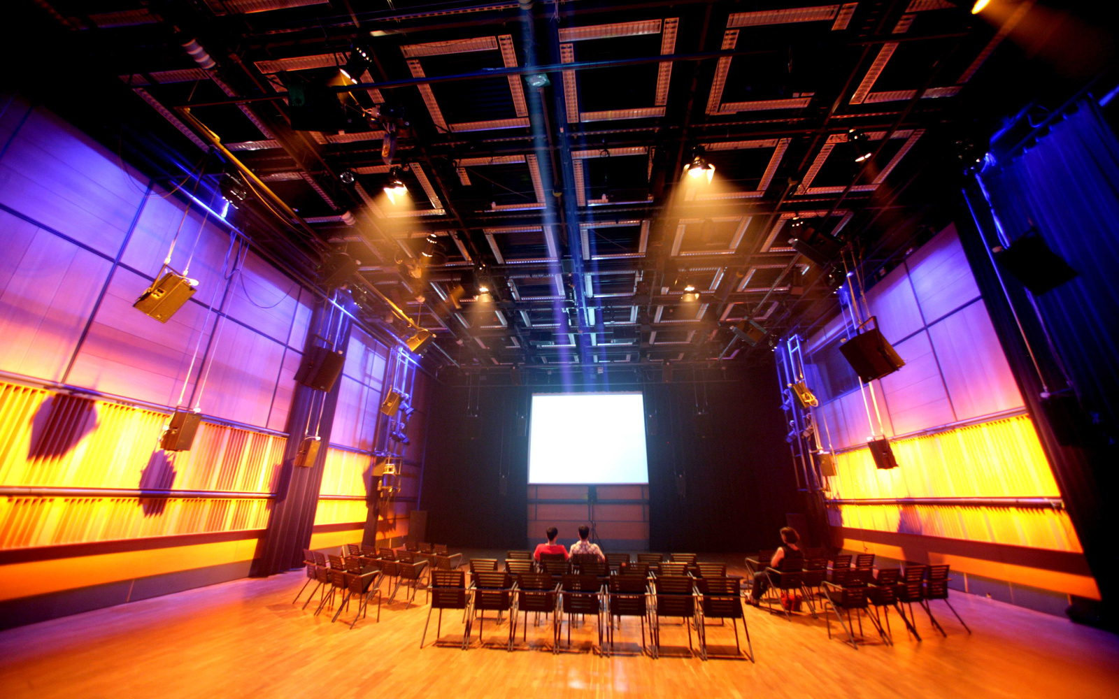 A white screen in the background. Previously, a number of chairs. The side walls are bathed in a purple and yellow light.