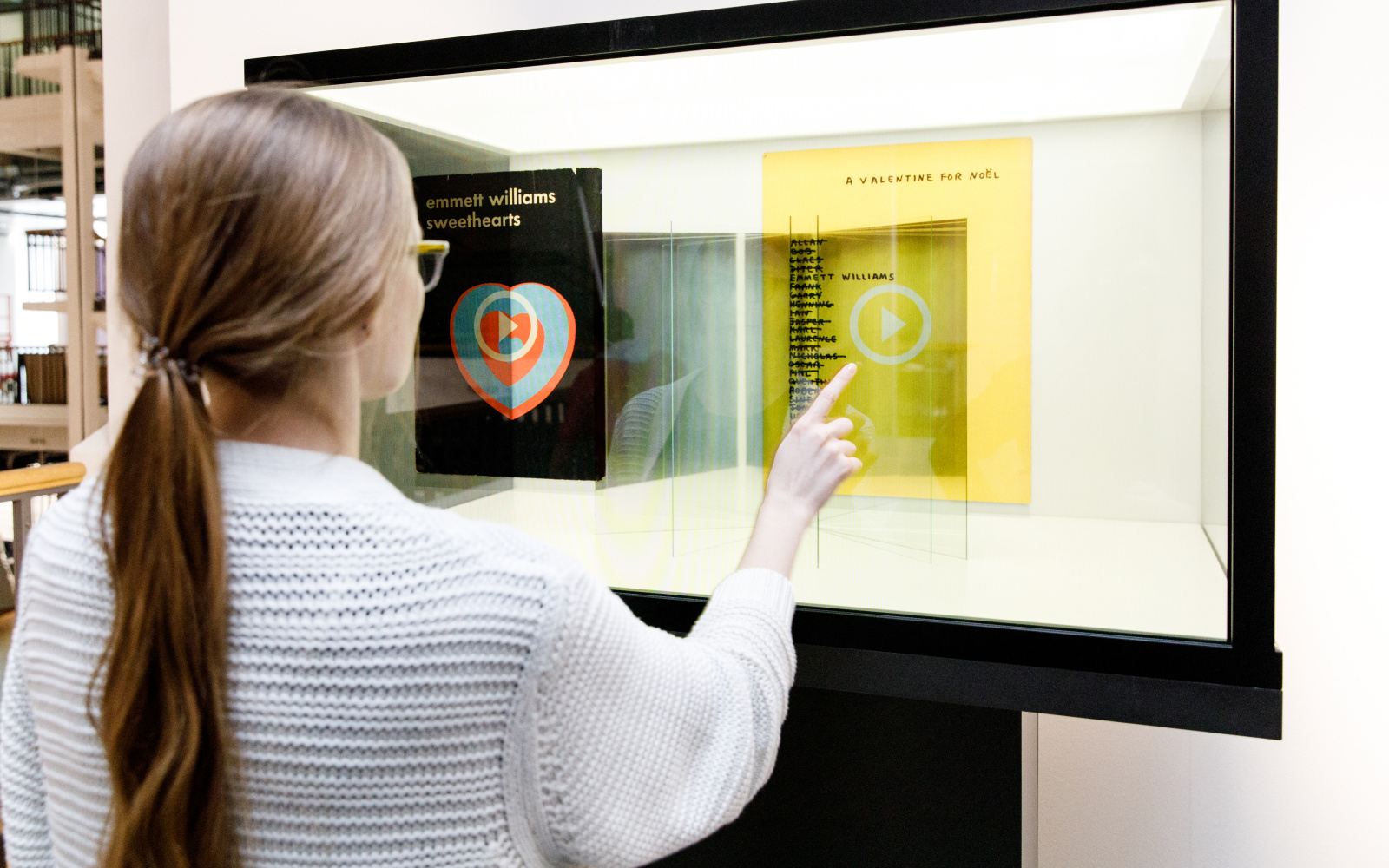 A woman stands in front of a glass box in which she can select and read books with her fingers.