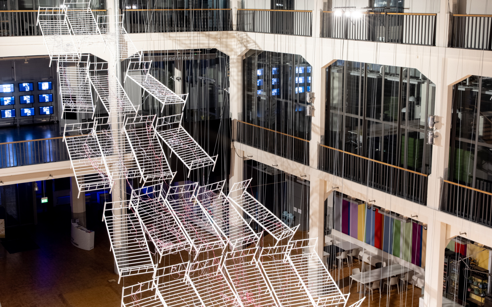 Installationsansicht von Chiharu Shiota`s Werk »Connected to Life«. Zu sehen sind aneinandergereihte, miteinander verbundene Bettgestelle, durchzogen von roten Schläuchen, die sich immer weiter vom Boden abheben und gemeinsam eine Art Weg aufwärts bilden.
