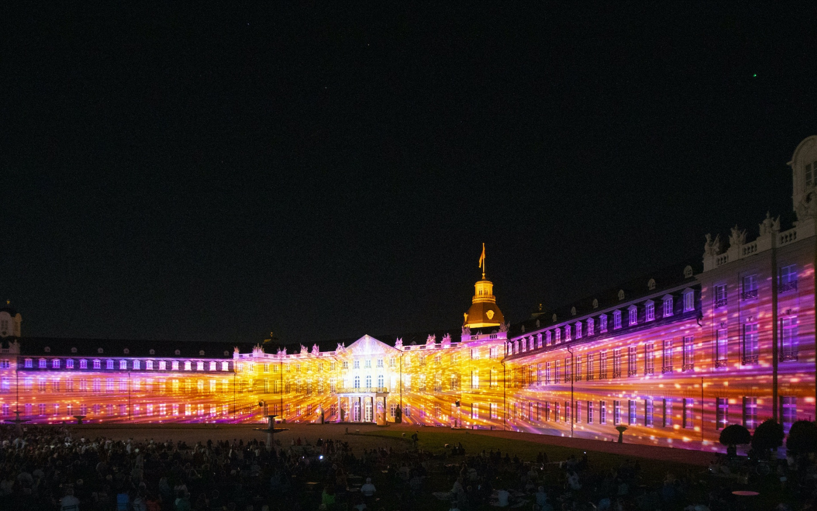 The facade of Karlsruhe Castle is illuminated in bright colors. It is night.