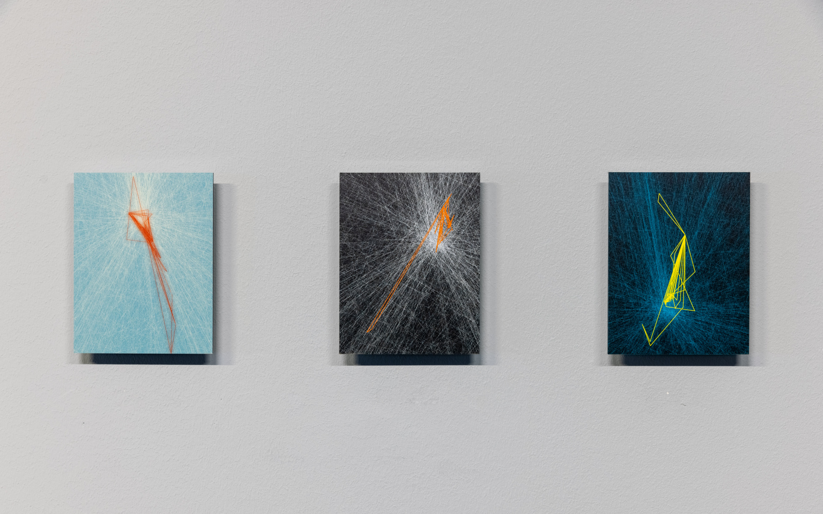 Three smaller canvases hang next to each other. They each show fine lines of a net. In Der Mitteist stands out in each case a thicker, colored, geometric-looking line shape.