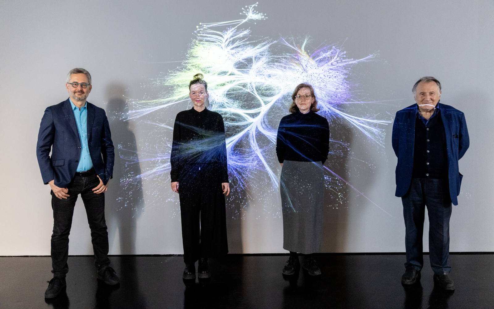 Four people stand in front of a projection of a network in the exhibition space. From left: Albert-László Barabási, Clara Runge, Teresa Retzer and Peter Weibel.