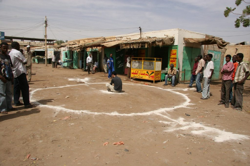 Artist Barış Seyitvan sits inside a white circle painted on the floor in a Sudanese village.