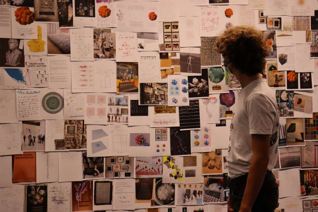 A teenager stands in front of a wall full of art sketches.