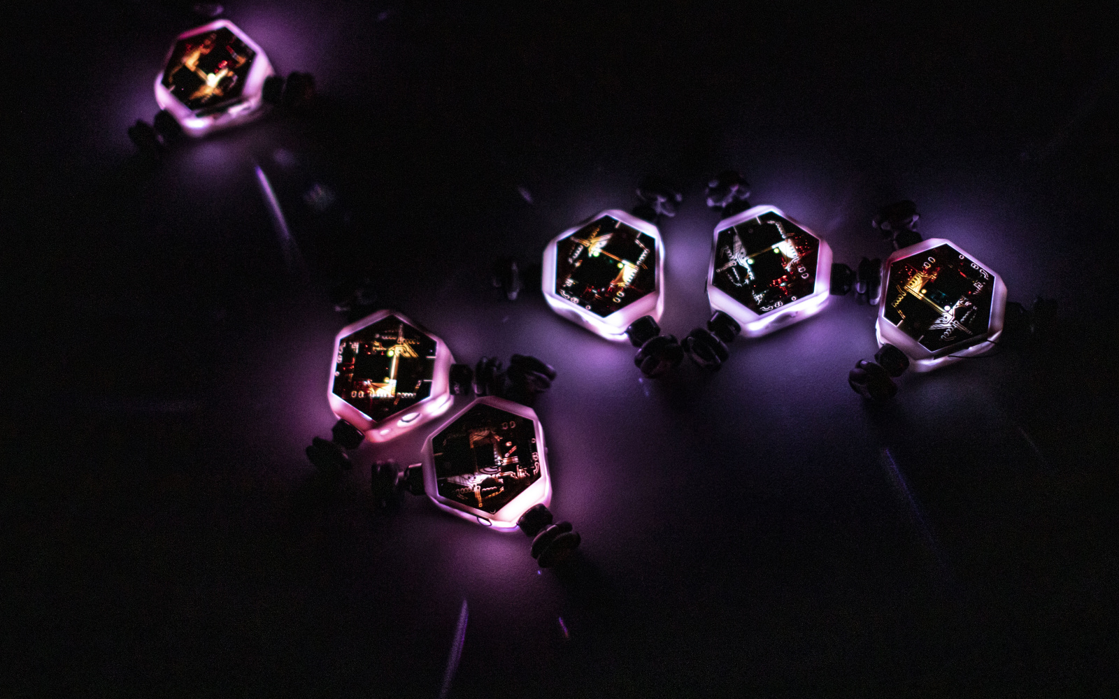 Leuchtende kleine Roboterkreisel bewegen sich auf dunklem Untergrund und interagieren miteinander.