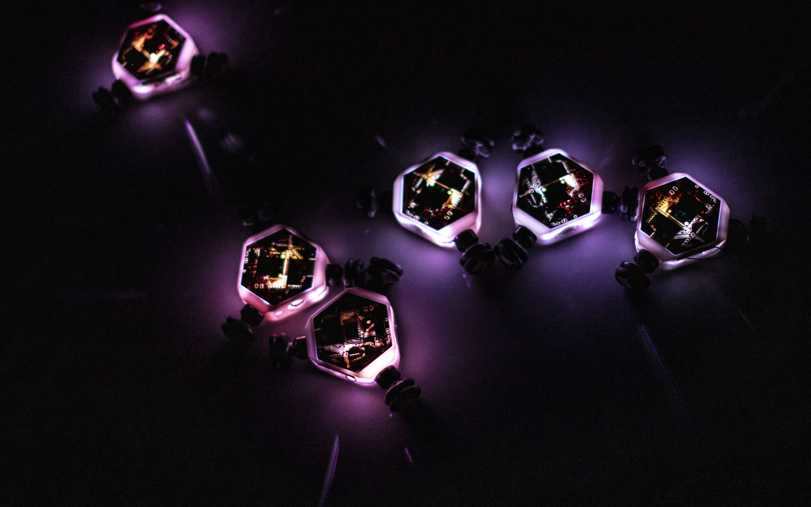 Glowing little robot spinning tops move on a dark background and interact with each other.