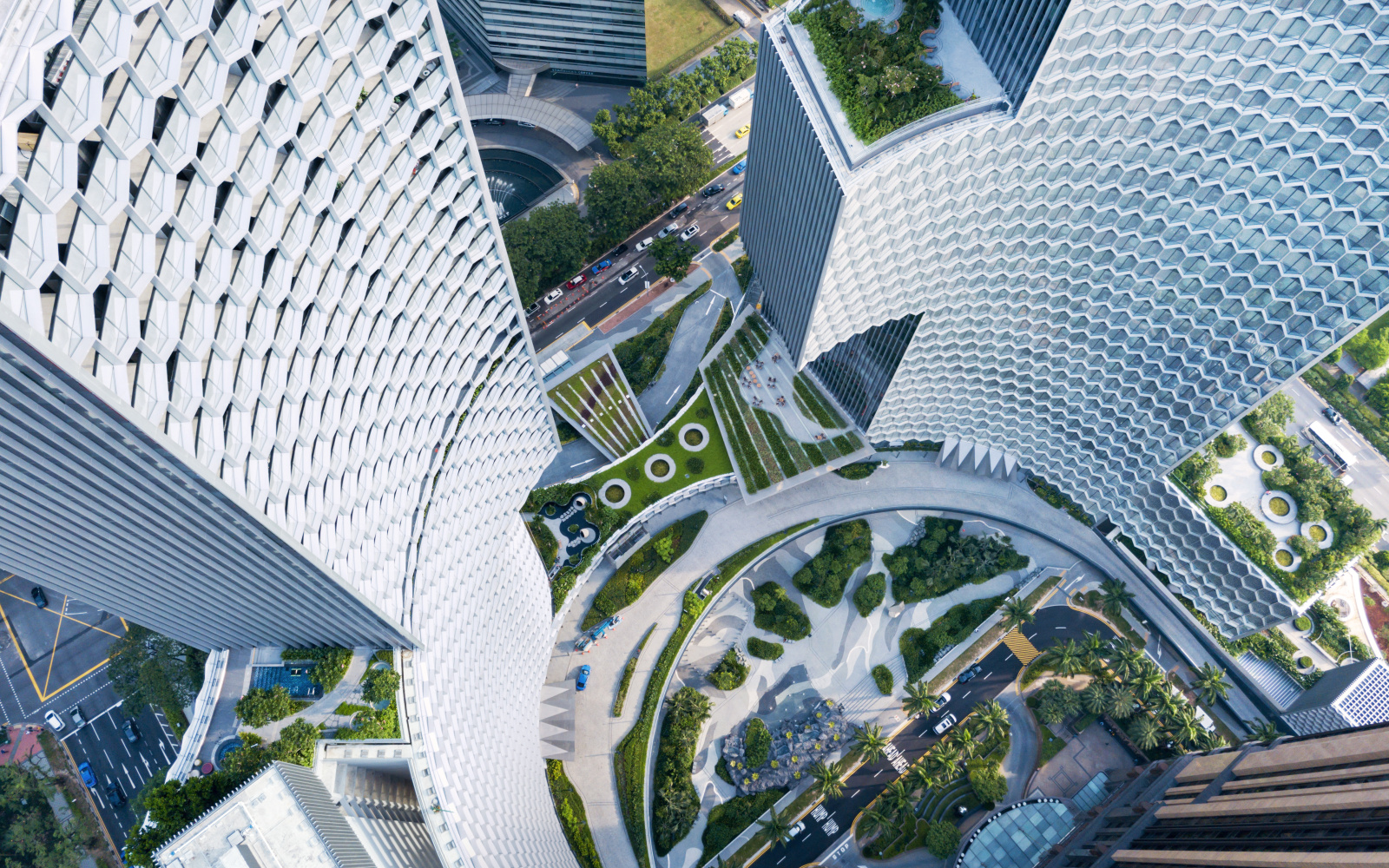 You can see a collection of tall buildings viewed from a bird's eye view. To the left and right at the top of the picture, the skyscrapers extend and surround an orderly park, which can be seen at the bottom of the picture. 