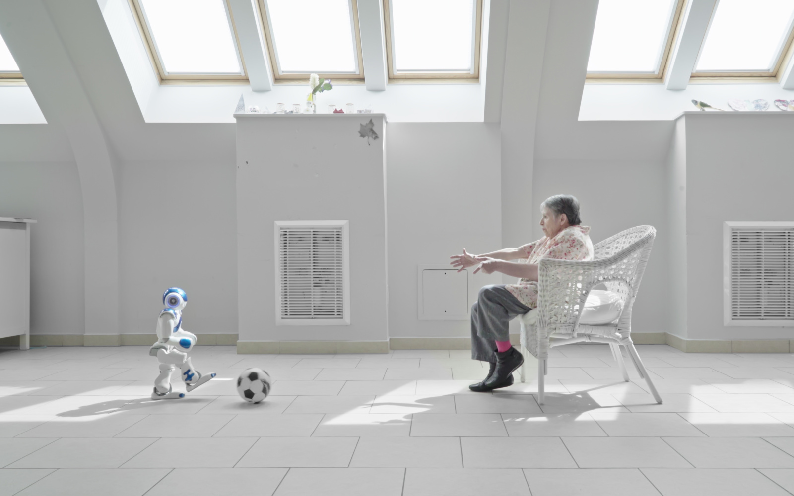 Ein kleiner humanoider Roboter spielt Fußball mit einer Seniorin in einem Pflegeheim.