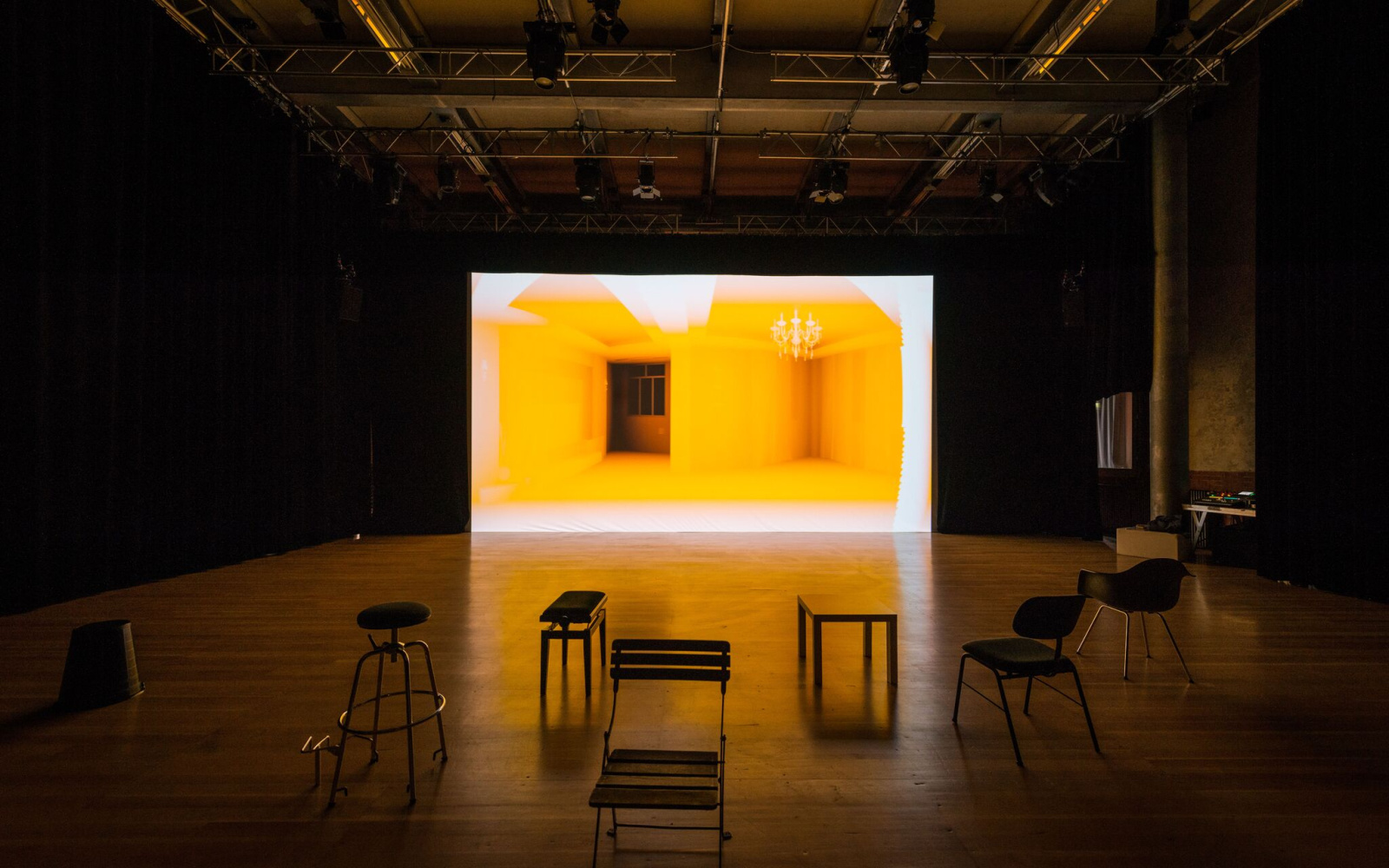 Exhibition view of the work »Homeschool« by Simone C. Niquille / Technoflesh in a darkened room, some seating and a large screen on which a yellow interior is projected