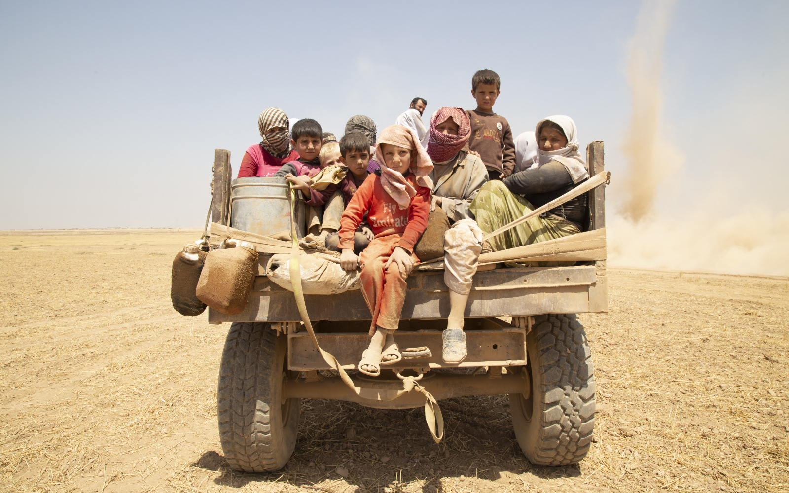 You can see many refugee children in the desert on a truck.