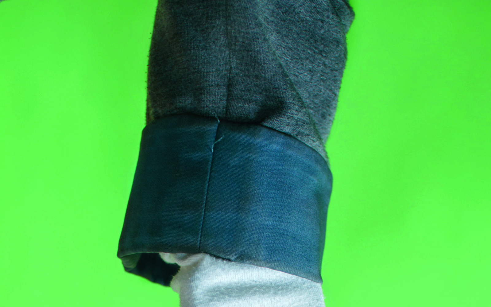 A woman's arm in close-up. The arm of a denim shirt is recognizable, underneath a longsleeve in which a cell phone is stuck. Then follows the hand, loosened.