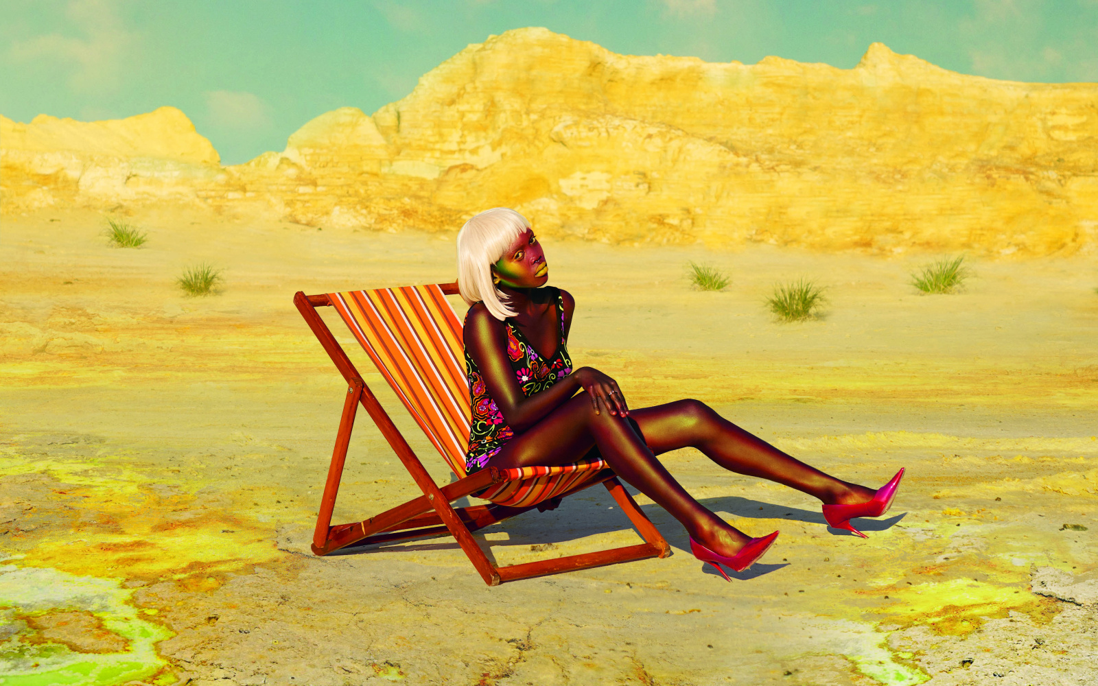 In einer bergigen Steppenlandschaft sitzt eine Frau, die wie ein Model aussieht, aufrecht in einem Sonnenstuhl.