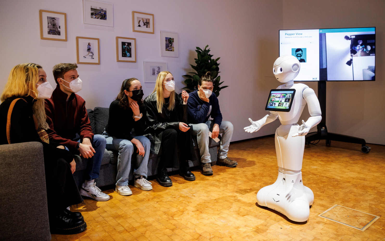 Menschen sitzen auf einem Sofa und ein Roboter steht vor ihnen