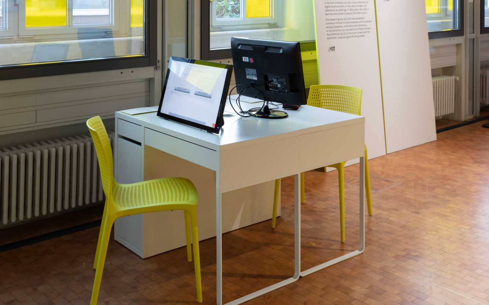 Ein Tisch mit zwei gelben Stühlen und zwei Bildschirmen