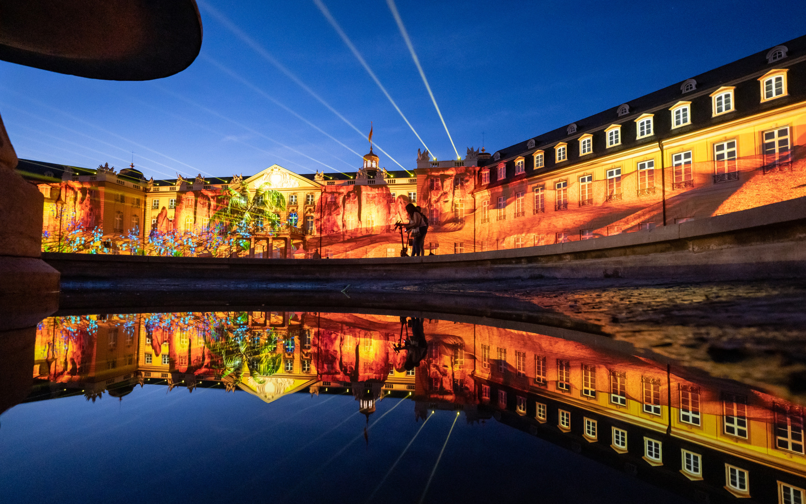 Zu sehen ist die beleuchtete Fassade des Karlsruher Barockschlosses in den Farben Orange und Gelb.