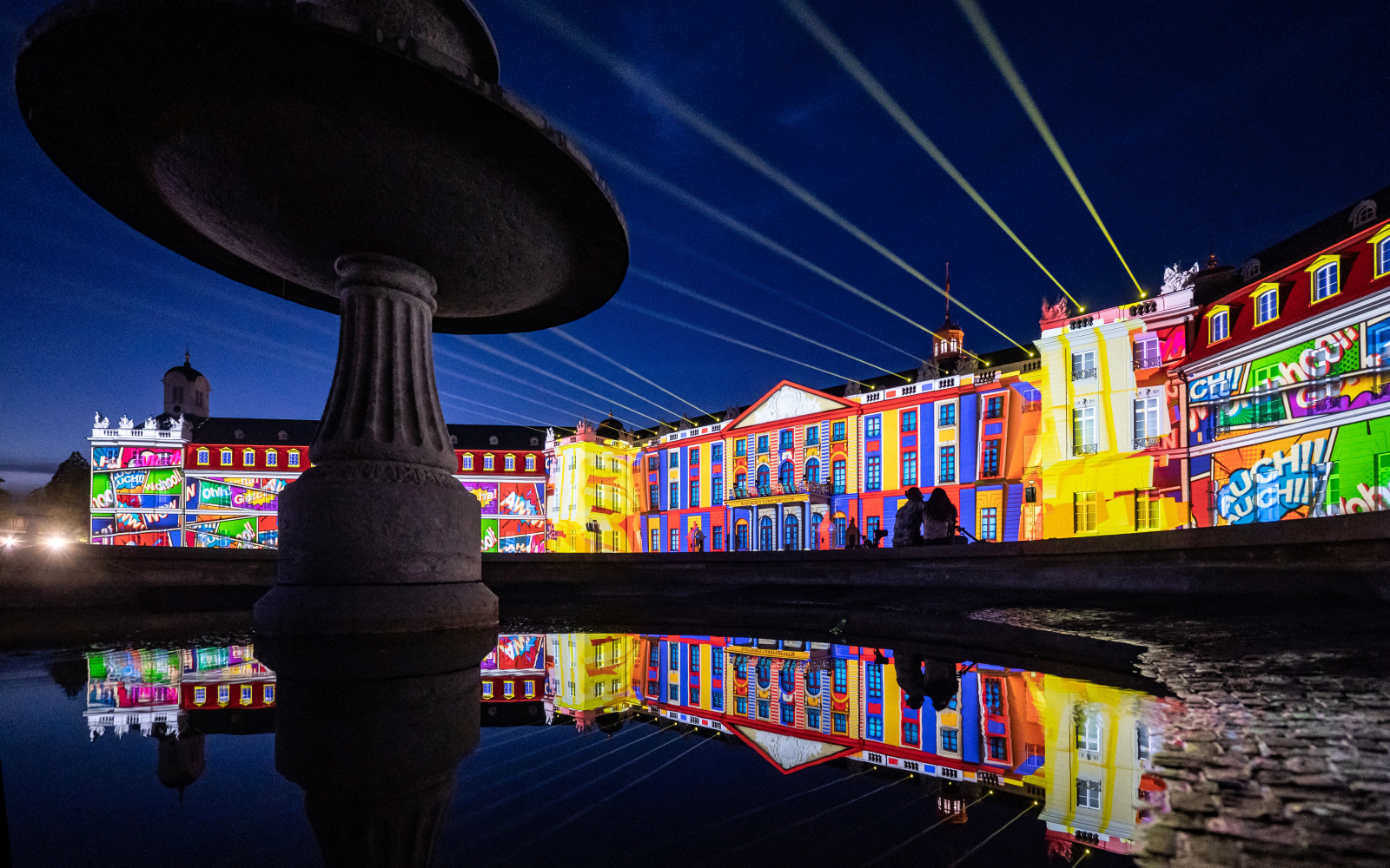 Zu sehen ist die bunt beleuchtete Fassade des Karlsruher Barockschlosses.