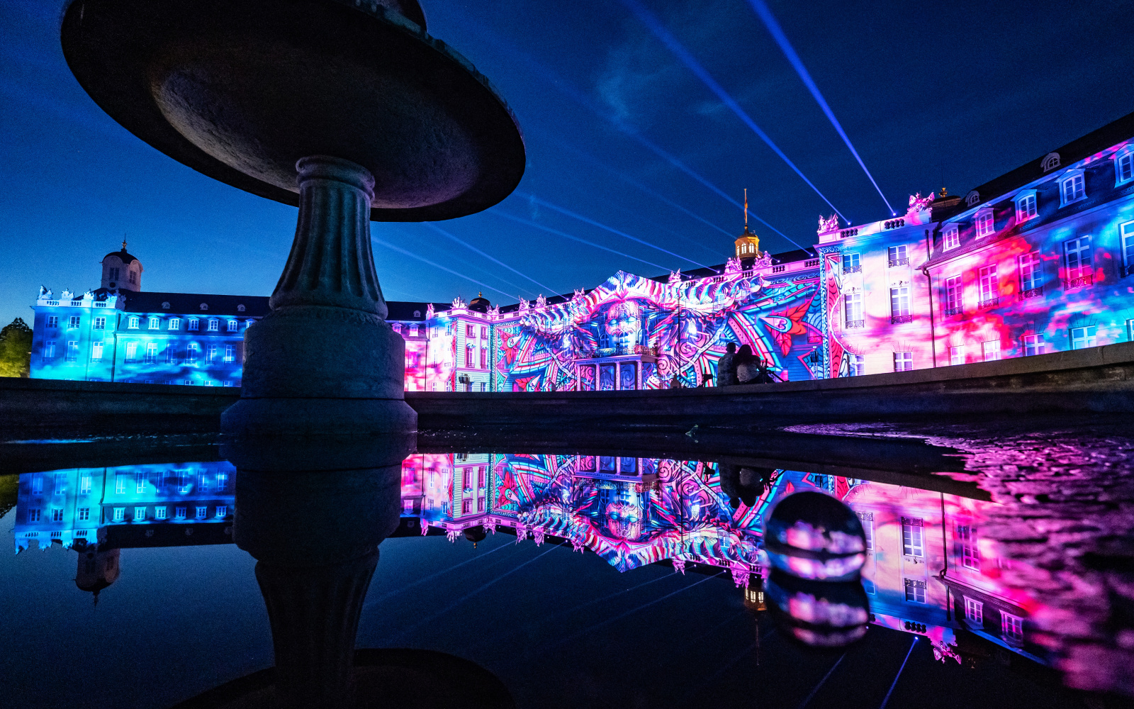 You can see the illuminated facade of the Karlsruhe Baroque Palace in the colors magenta and blue.