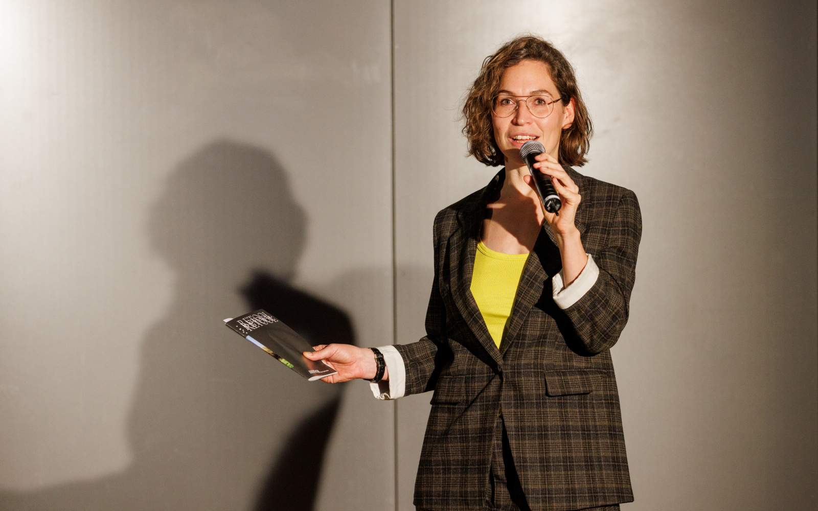 Zu sehen ist eine Person mit einem Mikrofon bei der Eröffnung der Ausstellung »Repairing the Present :RETOOL« 