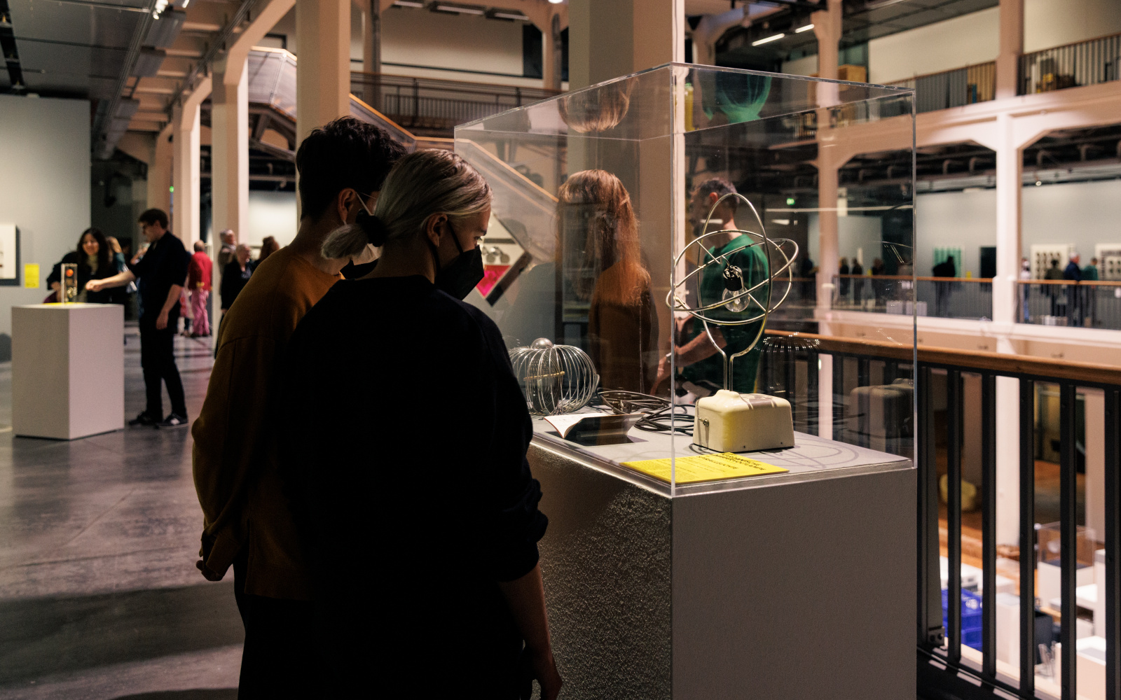 You can see two people looking at a glass box. In this glass box is a wire frame, in which a light bulb is attached.