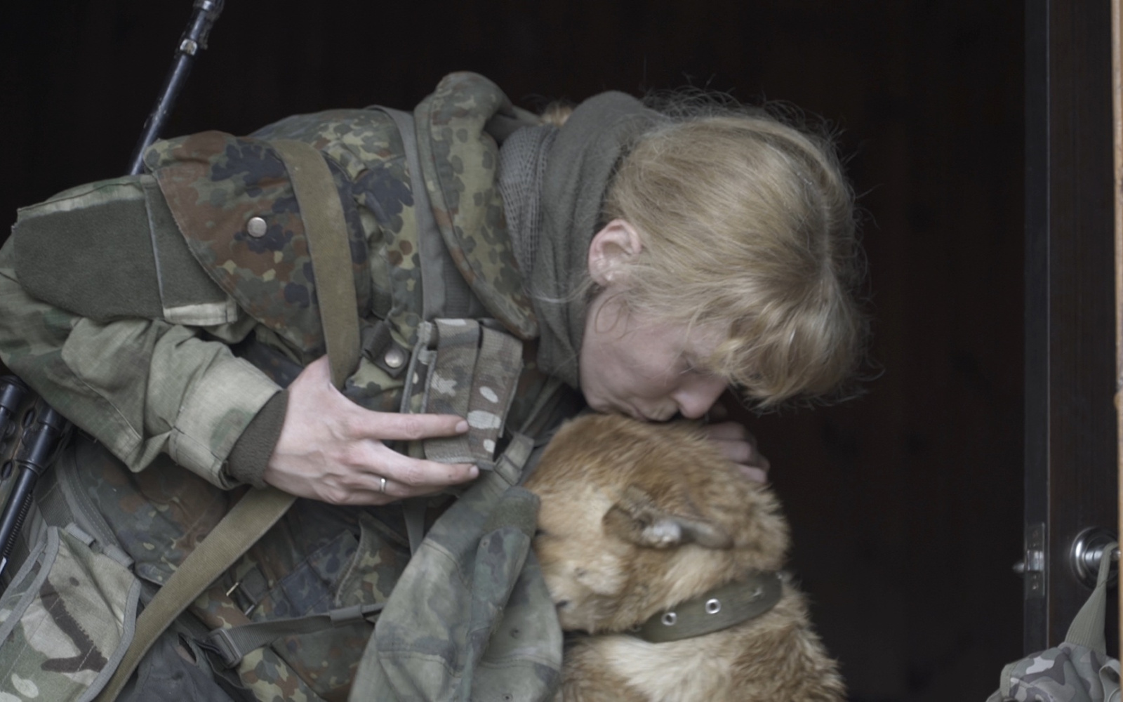 The picture shows a woman in camouflage colors caressing her dog.
