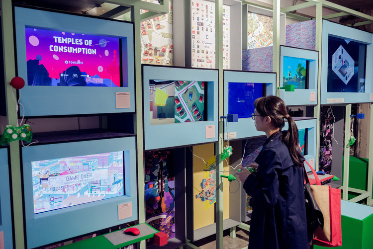 Person stands in front of several screens with a gaming controller