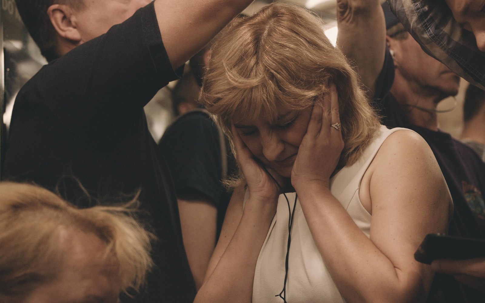 In the middle of the photo there is a woman in a crowd. She is the only person facing the camera, but she is looking down and holding her face in both hands.