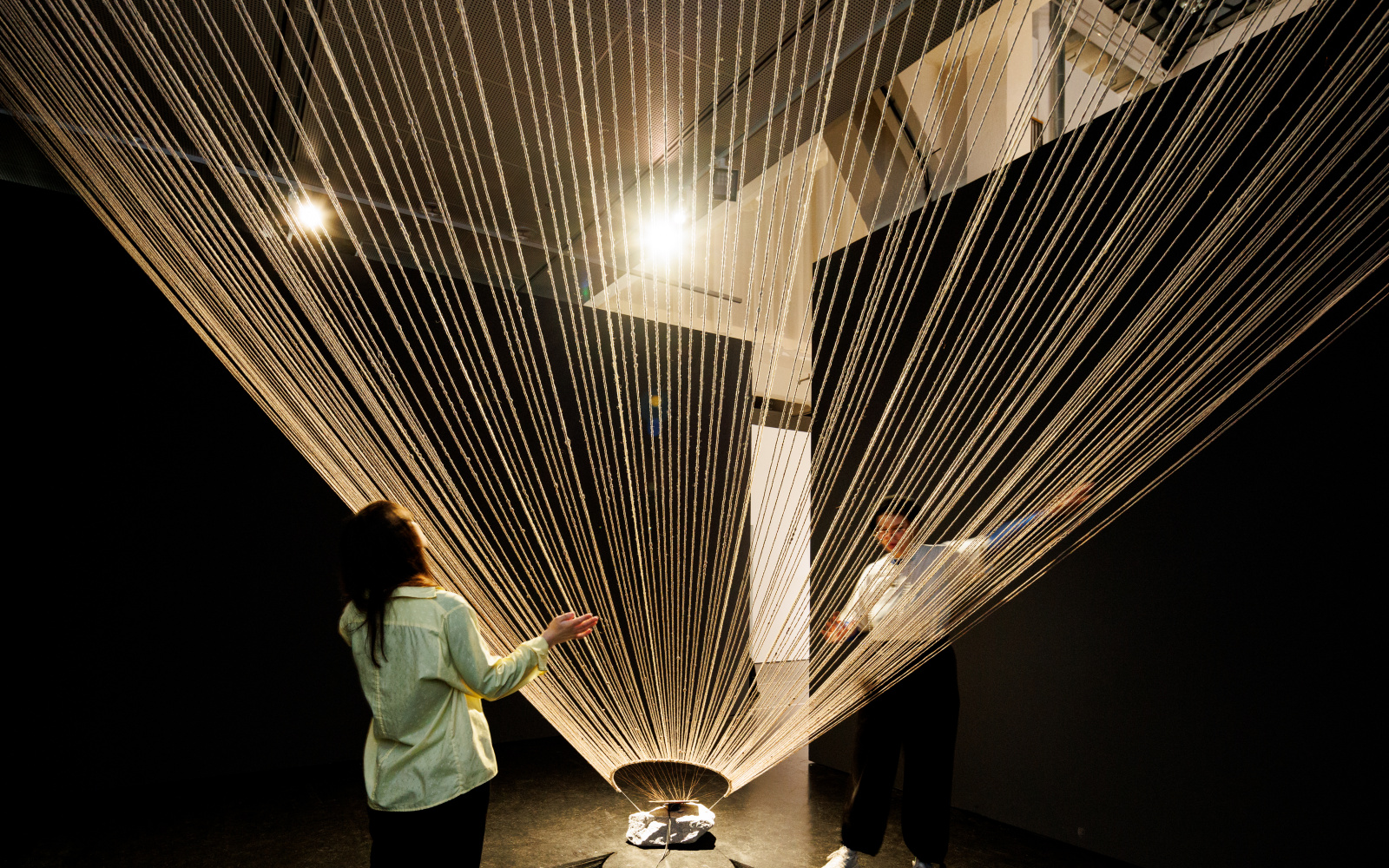 You can see a ceiling-high, wide net made of ropes. Two people are standing next to it, one on the left and one on the right.